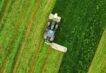 Aerial view of a tractor slashing a green paddock, leaving thick windrows of cut grass trailing behind