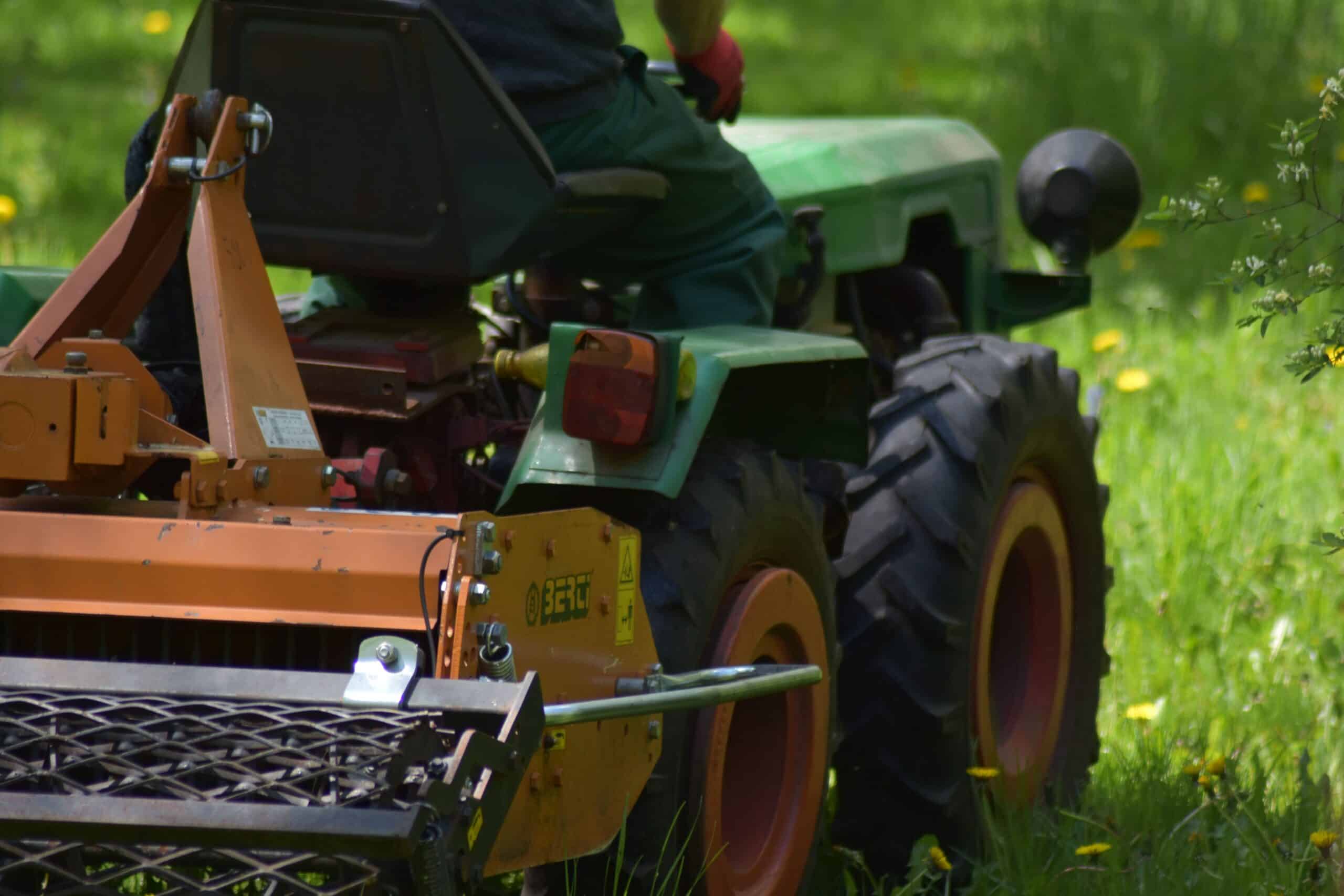 Close-up of a heavy-duty flail mower attachment on the back of a tractor, showing the protective steel housing and rear roller