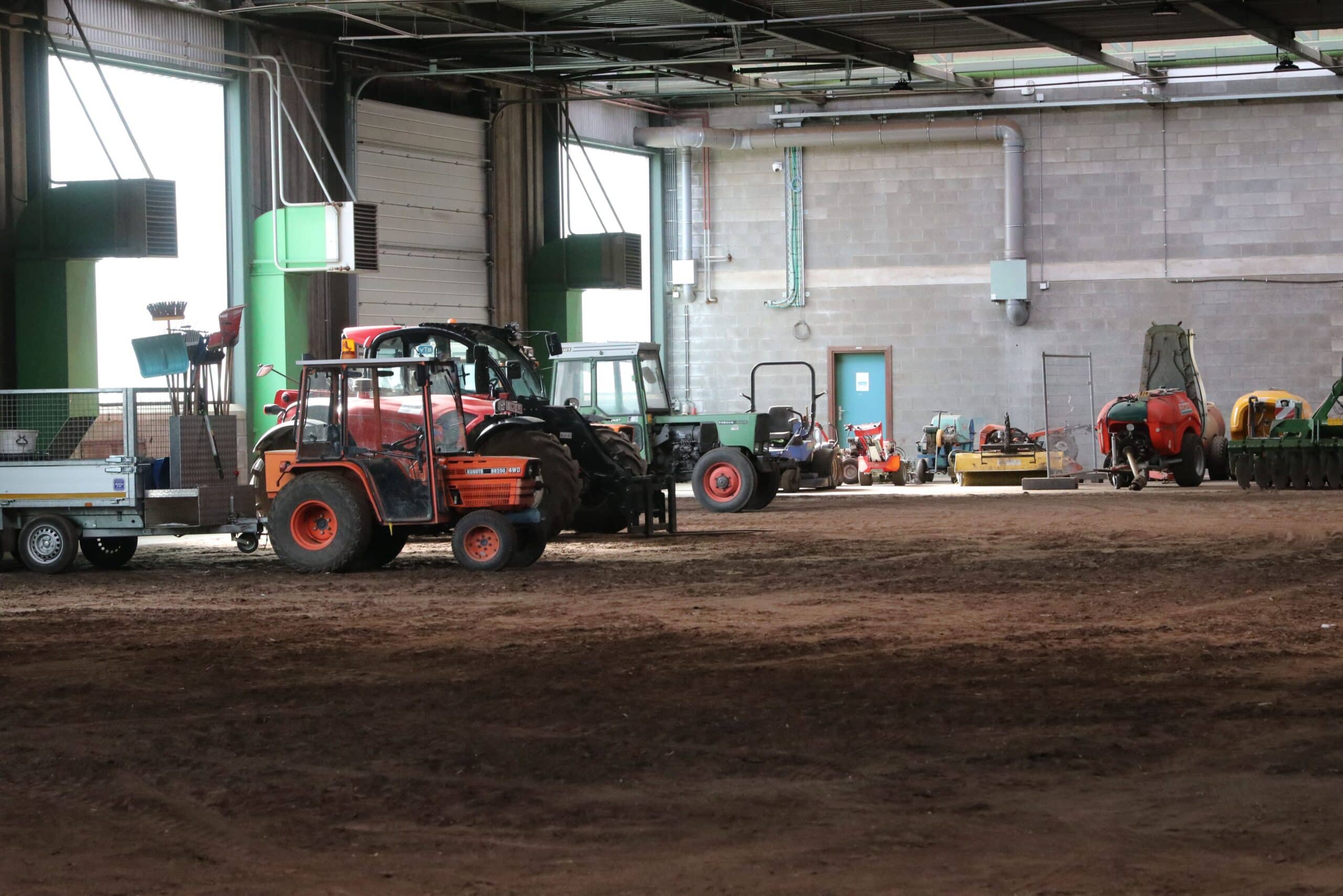 Wide view inside a large agricultural machinery workshop showing various tractors and farm implements parked inside